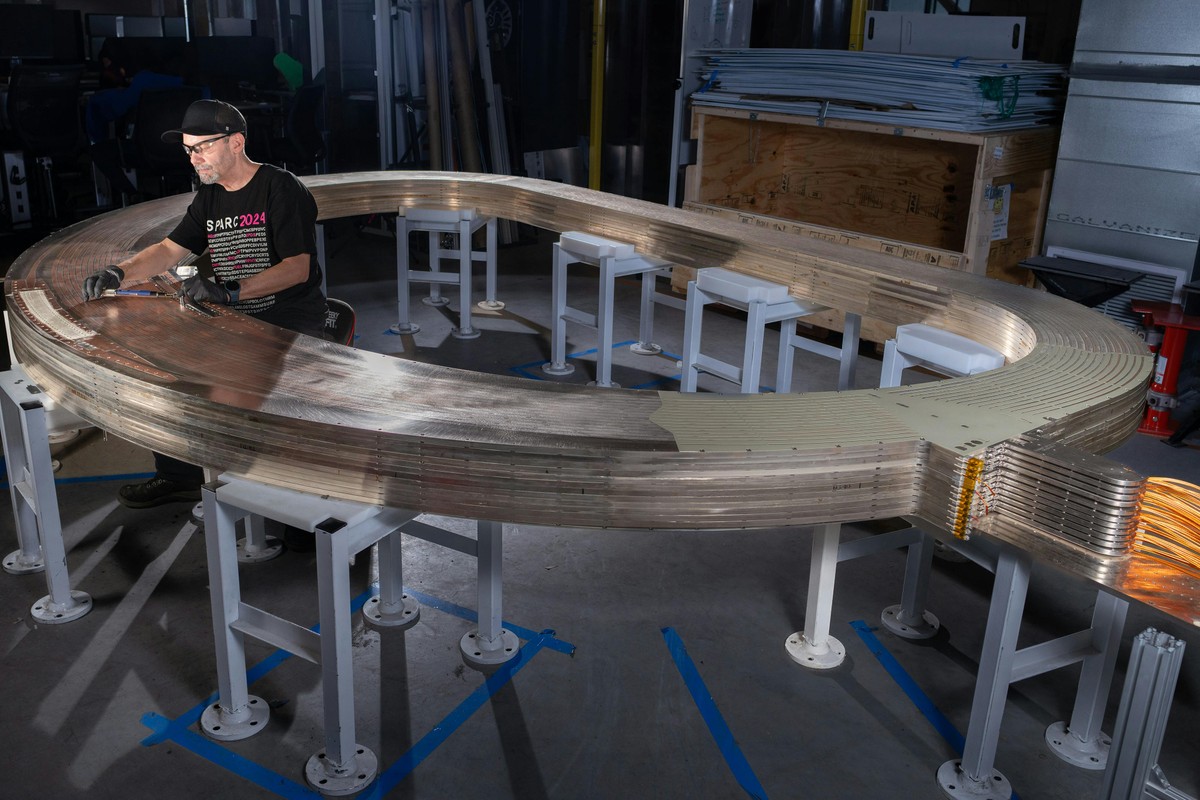 Male team member wearing a SPARC tshirt making measurements on a stack of d-shaped plates that form a fusion magnet.