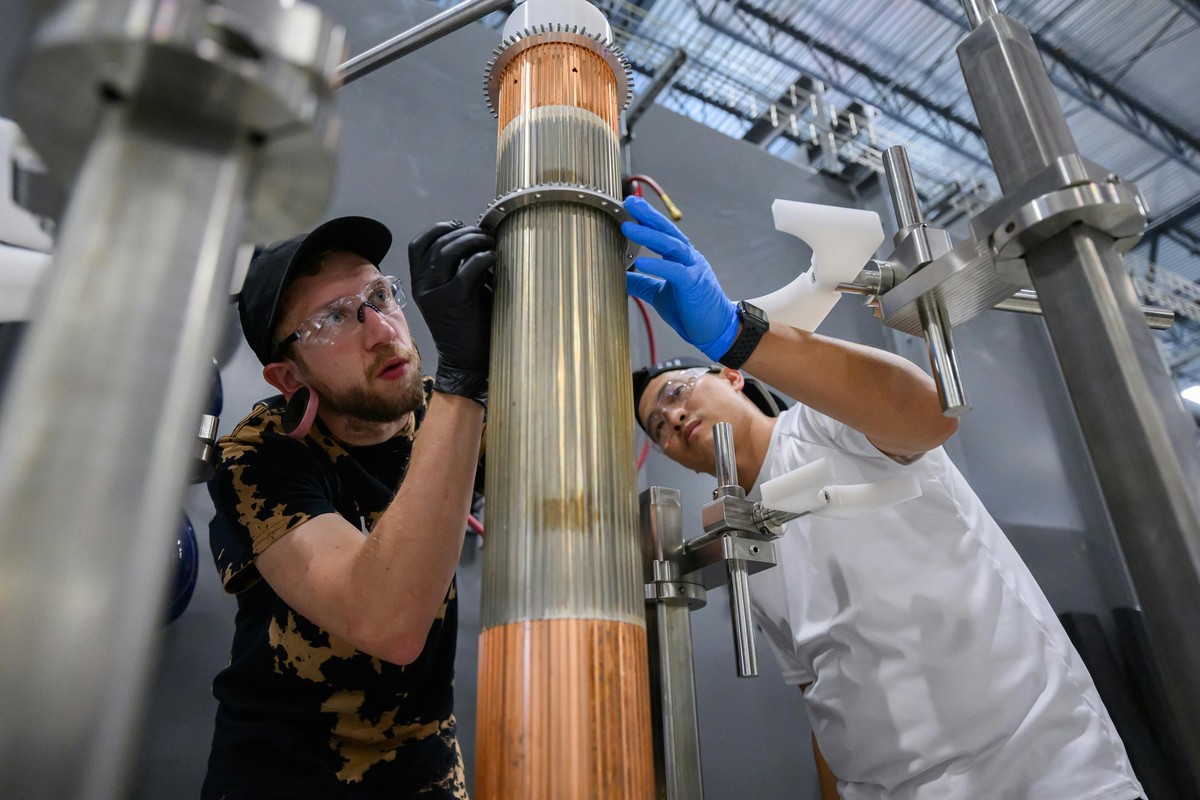 Two male team members setting a circular metal collar on a column with strips of silver and copper colours metal strips